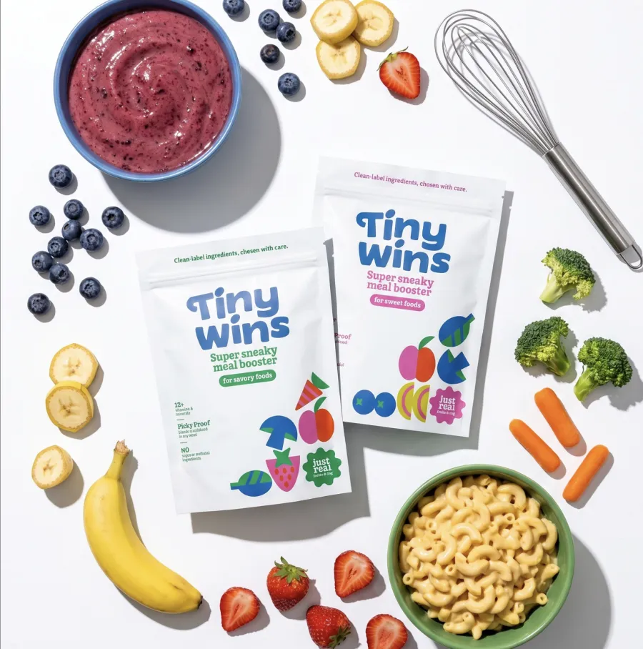 TinyWins meal-booster sachets photographed among fruit, vegetables and a bowl of pasta